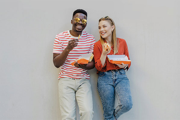 Two friends leaning against a wall eating